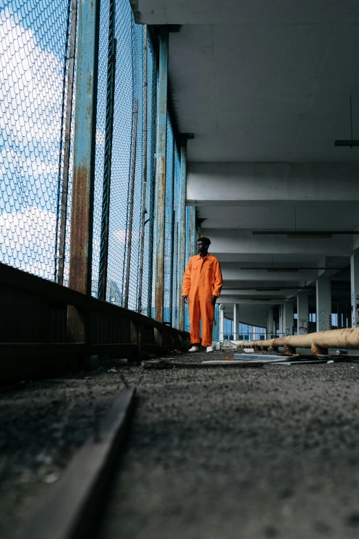 a man in an orange jumpsuit standing on a train track, inspired by Elsa Bleda, unsplash, in a prison cell, standing on ship deck, street clothing, reflective suit