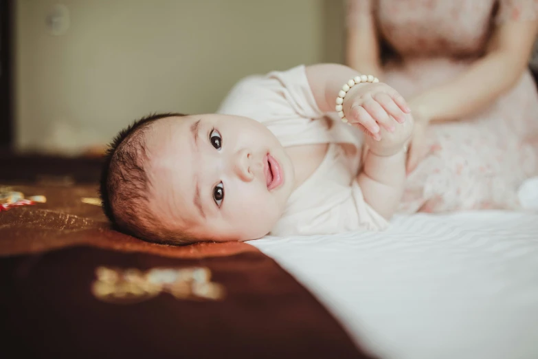 a close up of a baby laying on a bed, unsplash, hurufiyya, jewelry, japanese, extremely realistic photo, portrait photo