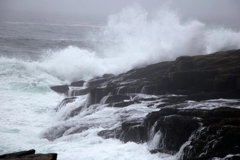 a man standing on top of a rocky cliff next to the ocean, by David Donaldson, pexels, hurufiyya, in rough seas with large waves, dense rain, slide show, 2022 photograph