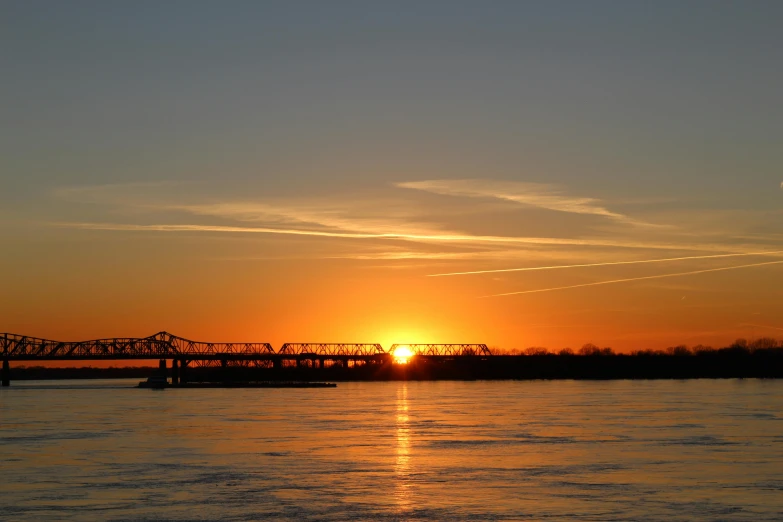 a large body of water with a bridge in the background, by Joe Stefanelli, sun sunset, memphis, cold sunny weather, 2 0 2 2 photo