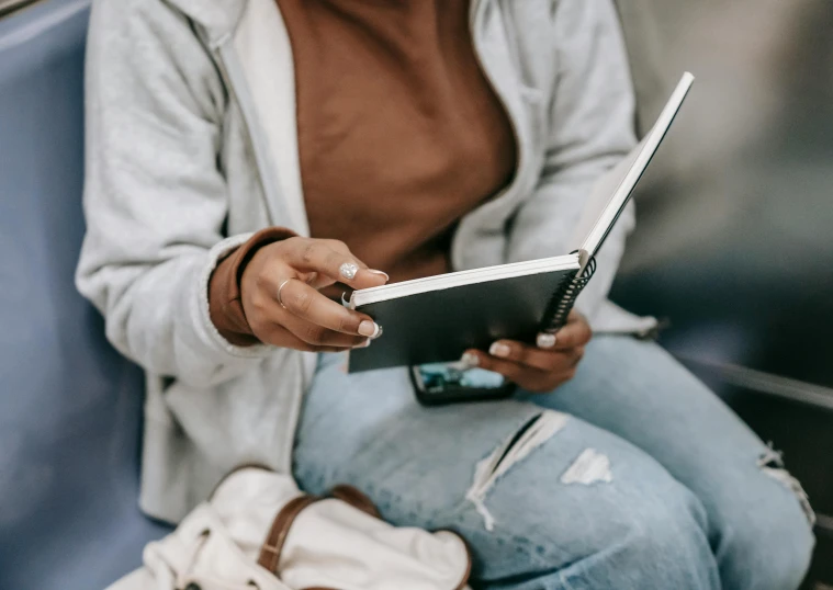 a woman sitting on a train reading a book, trending on pexels, wearing jeans and a black hoodie, white sketchbook style, holding notebook, pastel'
