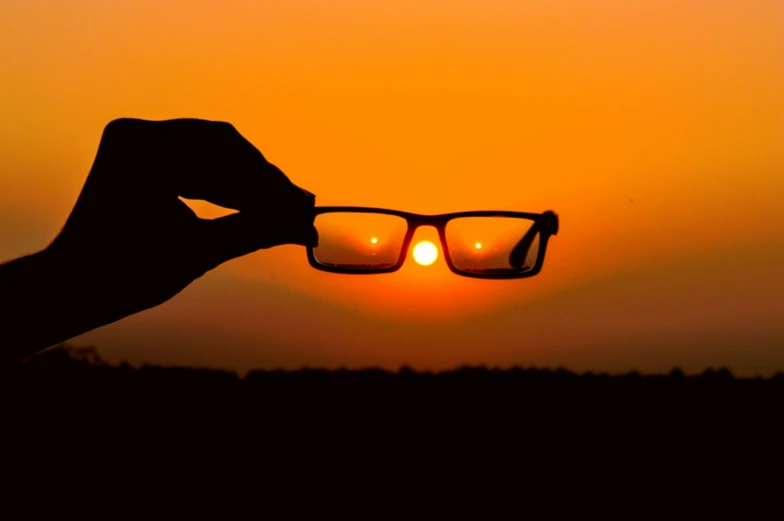 a person holding up a pair of glasses at sunset, square rimmed glasses, ((sunset)), suns, high resolution