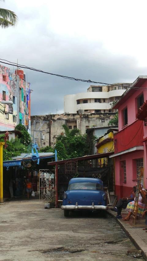 a blue car parked in front of a pink building, inspired by Francis Souza, graffiti, ancient ruins favela, wet market street, panoramic shot, faded red and yelow