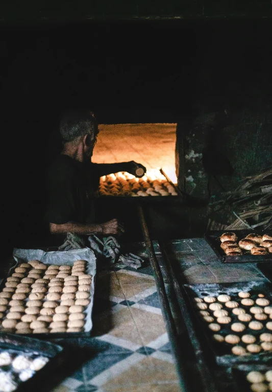 a man standing in front of an oven filled with doughnuts, by Daniel Lieske, pexels contest winner, old town mardin, cookies, inside primitive hut, in sao paulo