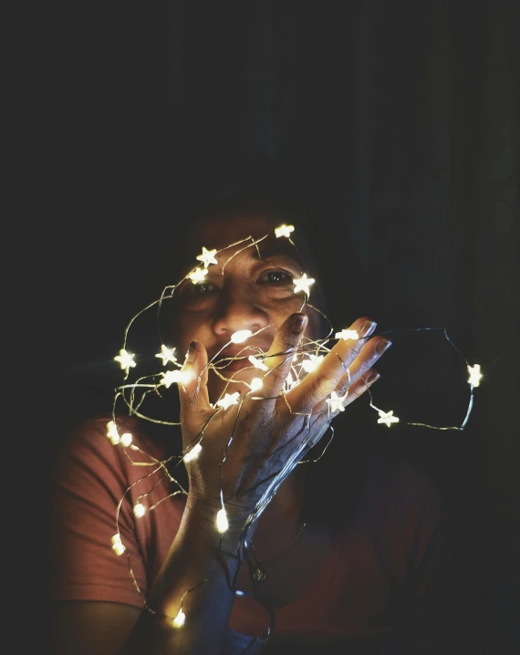 a woman holding a string of lights in front of her face, pexels, light and space, instagram post, tiny stars, happy and spirited expression, grainy photo