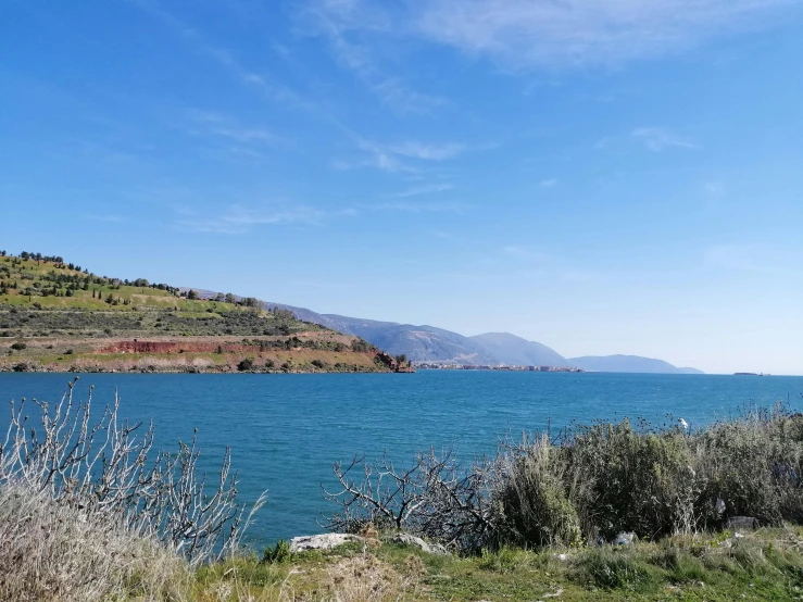 a large body of water sitting next to a lush green hillside, a picture, unsplash, les nabis, greek setting, ((rust)), lake blue, near the beach