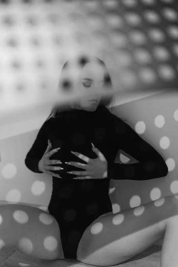 a black and white photo of a woman sitting on a couch, inspired by Man Ray, unsplash, surrealism, dots abstract, hands behind her body pose!, light leak, wearing a black bodysuit