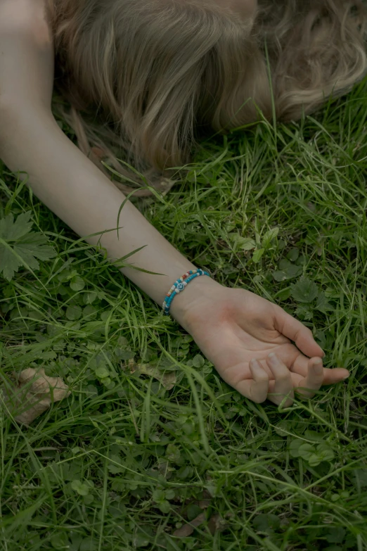 a woman laying on top of a lush green field, an album cover, inspired by Elsa Bleda, deviantart, neon hand sports bracelet, thin blue arteries, it follows :7, jewelry