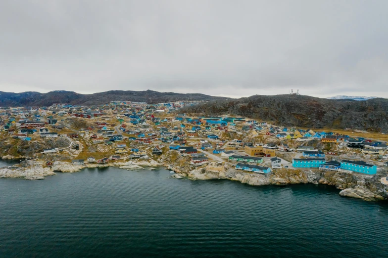 a large body of water next to a small town, trending on unsplash, hurufiyya, inuit heritage, colorful houses, view from helicopter, camps in the background