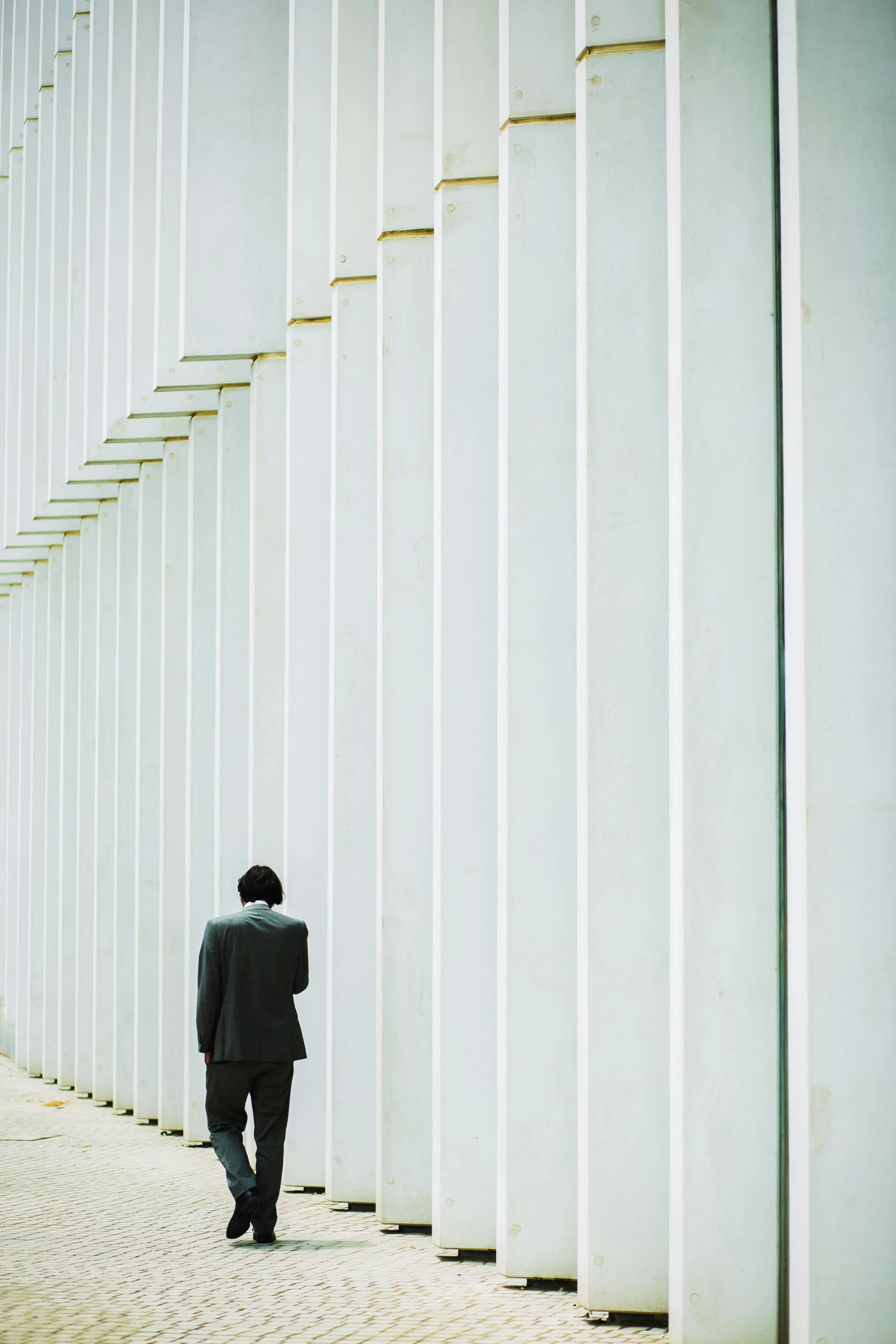 a man in a suit standing in front of a wall, inspired by David Chipperfield, unsplash, postminimalism, many columns, spying, hunched over, square lines