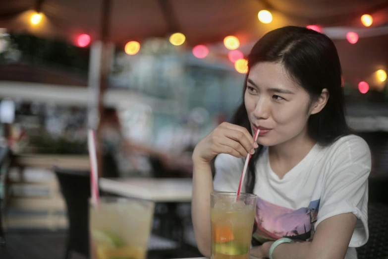 a woman sitting at a table with a drink in her hand, by Tan Ting-pho, pexels contest winner, young cute wan asian face, with a straw, profile image, flashing lights