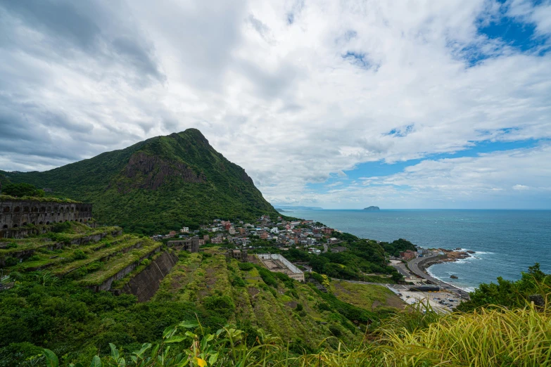 a lush green hillside next to the ocean, a picture, unsplash contest winner, mingei, hashima island, volcano valley, village in the background, multiple stories