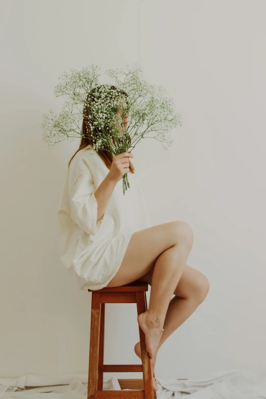 a woman sitting on a stool holding a bunch of flowers, inspired by Elsa Bleda, trending on unsplash, aestheticism, all white, woman made of plants, flower mask, thigh focus