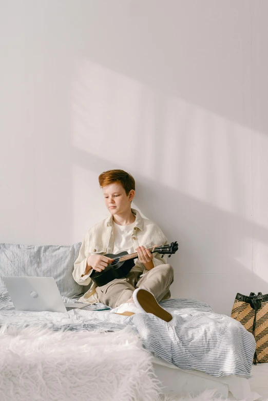 a man sitting on a bed playing a guitar, trending on pexels, visual art, red haired teen boy, wearing white pajamas, androgynous person, playing a mandolin