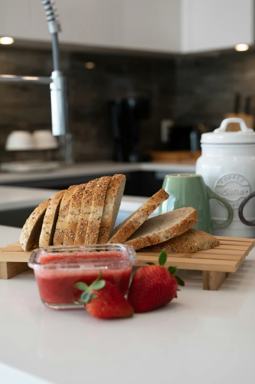 a counter topped with slices of bread next to a bowl of strawberries, dwell, lynn skordal, breakfast, jars