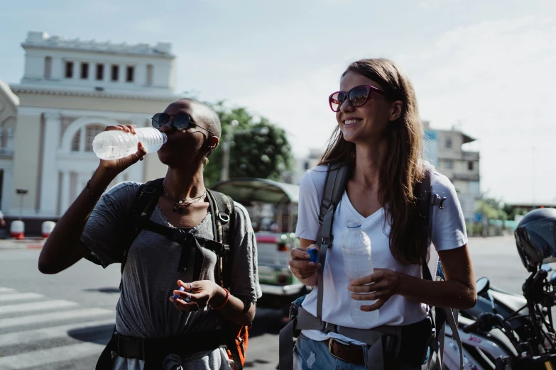 a couple of women standing next to each other on a street, pexels contest winner, hydration, guide, profile image, with a backpack