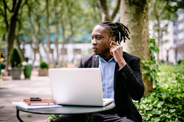 a man sitting at a table talking on a cell phone, trending on pexels, laptops, against the backdrop of trees, afro tech, serious business