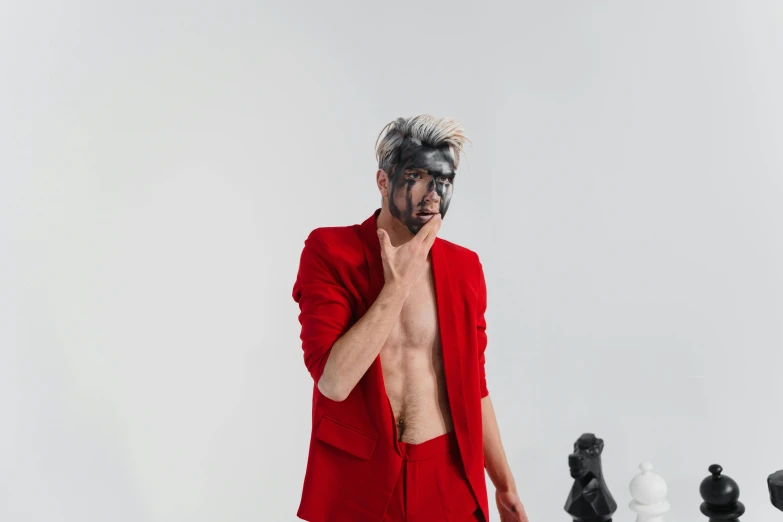 a man in a red suit standing next to chess pieces, an album cover, inspired by Alonso Vázquez, trending on pexels, aestheticism, white man with black fabric mask, a silver haired mad, bodypainting, his hair is messy and wild