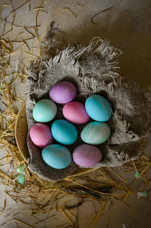 a basket filled with eggs sitting on top of a table, a pastel, mauve and cinnabar and cyan, tie-dye, rustic setting, petite