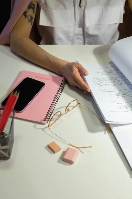 a woman sitting at a table with a notebook and pen, an album cover, trending on pexels, academic art, pink, low quality photo, classroom, zoomed in