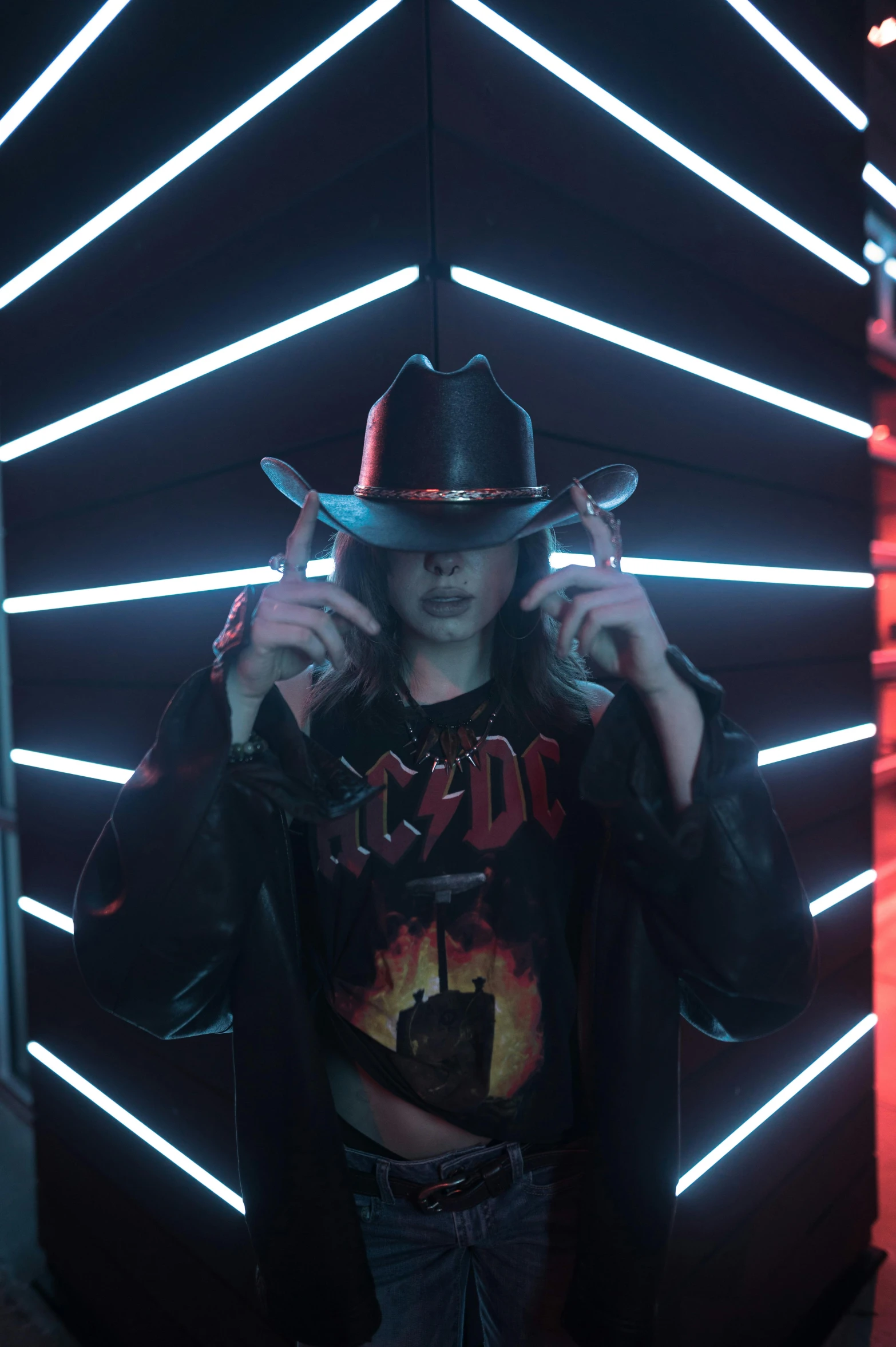 a man standing in front of a wall with neon lights, an album cover, pexels, holography, wearing a cowboy hat, witchcore, power pose, e-girl