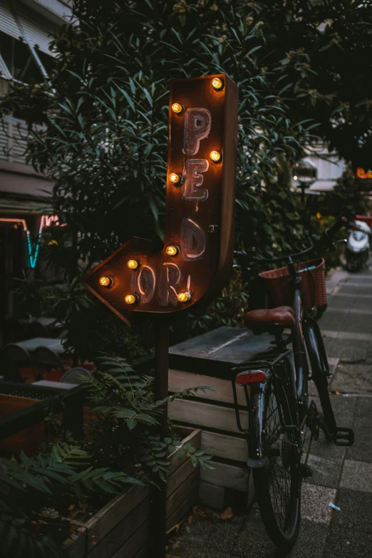 a bicycle parked on the side of a street, by Matt Cavotta, pexels contest winner, happening, retro lights, sign, cafe, lush tress made of city lights