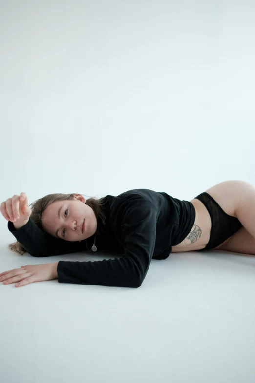 a woman in a black top laying on the floor, non binary model, white backdrop, bum, exposed midriff