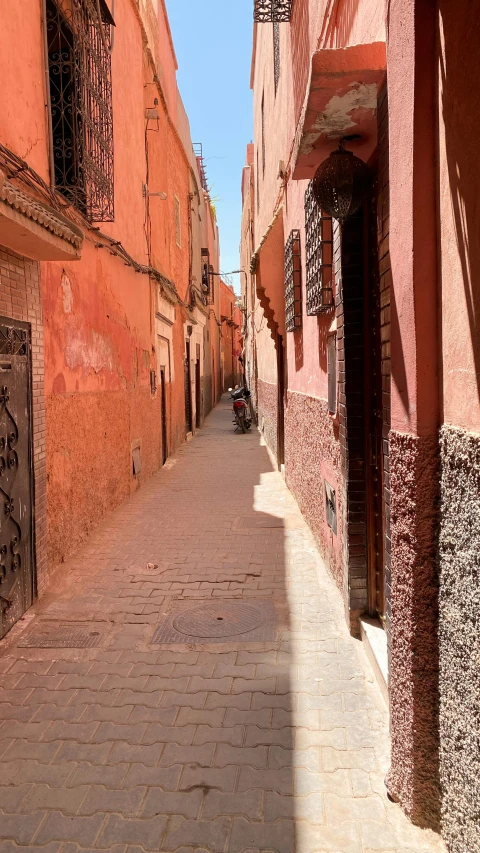 a person riding a bike down a narrow street, by Riad Beyrouti, pexels contest winner, les nabis, red wall, sunny day, square, with an intricate