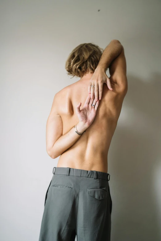 a shirtless man standing in front of a white wall, unsplash, showing her shoulder from back, stretch, teenage boy, anatomical