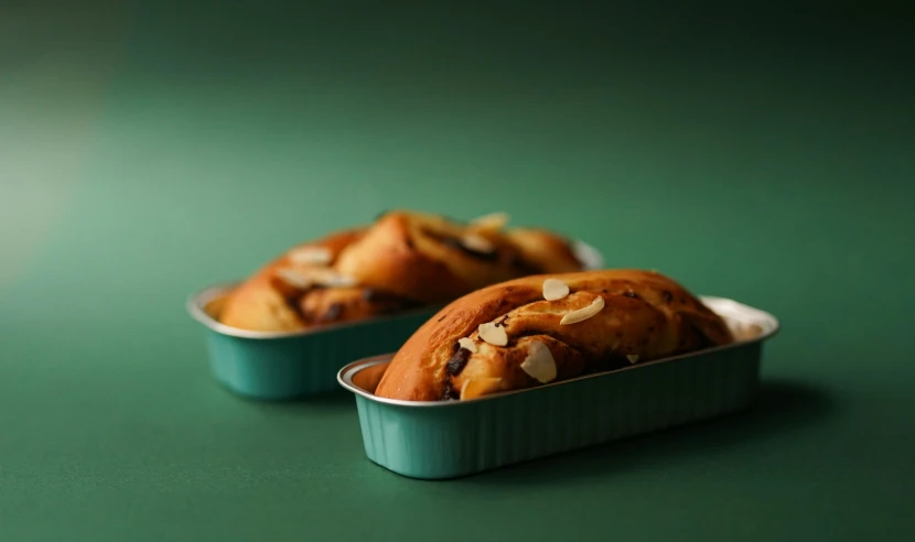 two pastries in tins on a green surface, inspired by Richmond Barthé, unsplash, hurufiyya, medium shot angle, brown, view from the side, kek