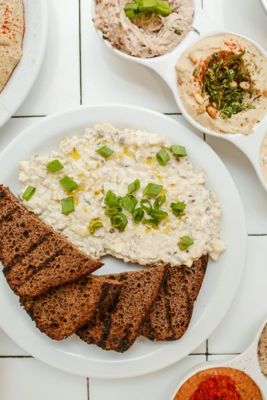 a table topped with lots of different types of food, dau-al-set, toast, sleek white, humus, hemp