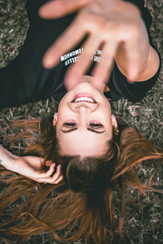 a woman laying on top of a grass covered field, by Niko Henrichon, trending on pexels, happening, sarcastic smile showing teeth, in love selfie, hands straight down, ( redhead