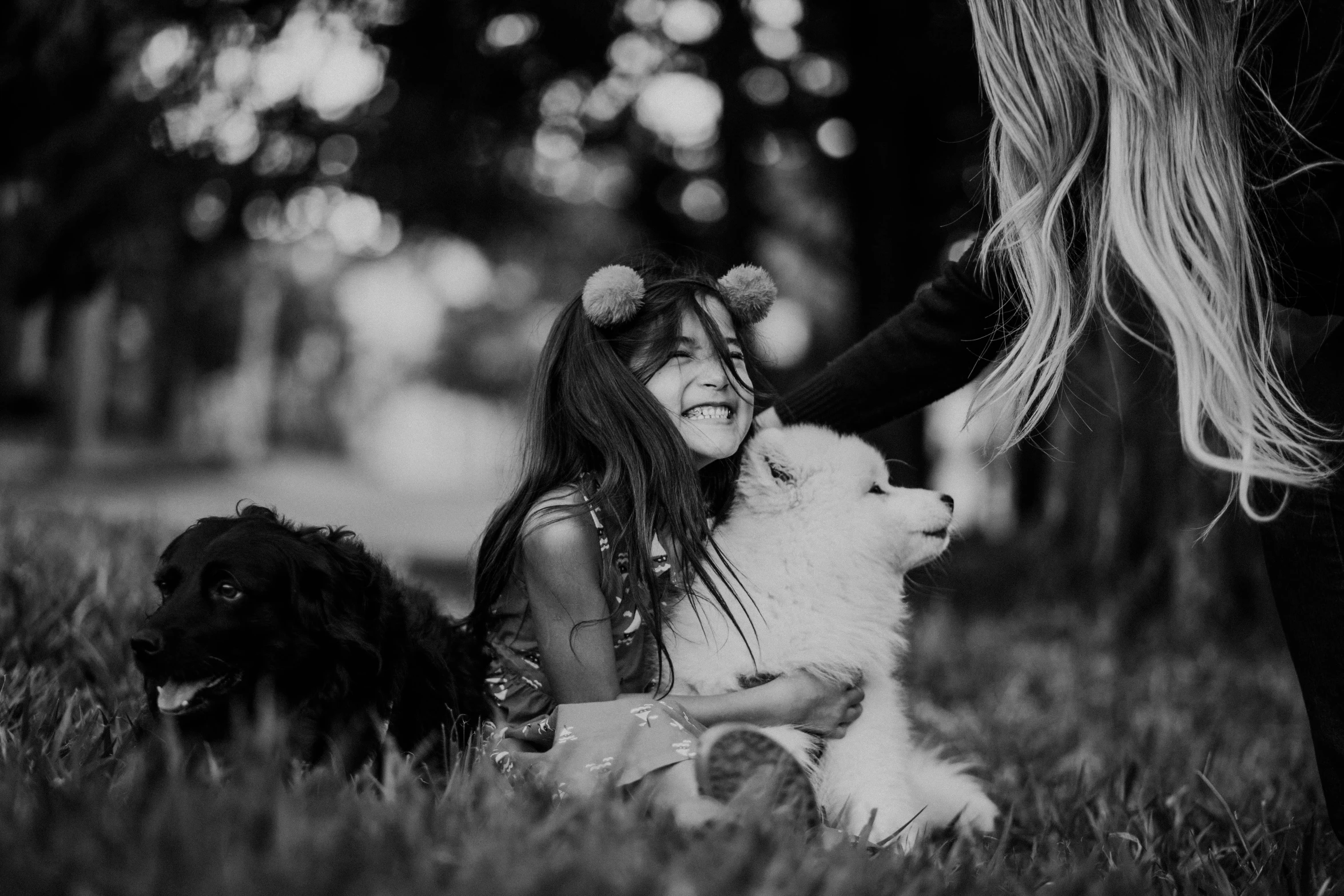 a woman sitting in the grass with two dogs, a black and white photo, by Emma Andijewska, pexels contest winner, happy kid, samoyed dog, alena aenami and lilia alvarado, avatar image