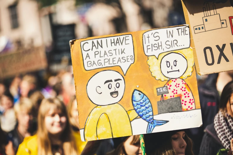 a group of people holding signs in front of a crowd, a cartoon, by Julia Pishtar, trending on unsplash, plasticien, fish man, made of cardboard, sustainable materials, parade