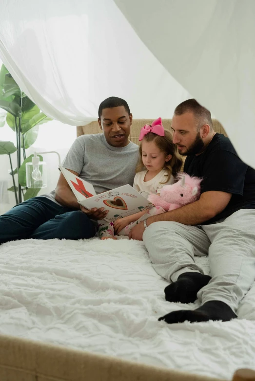 a group of people sitting on top of a bed, stuffed animal, a book, with a kid, profile image