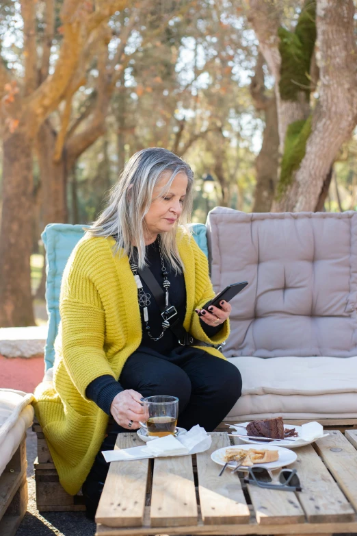 a woman sitting on top of a wooden table next to a couch, mobile app, eating outside, manuka, karen carr