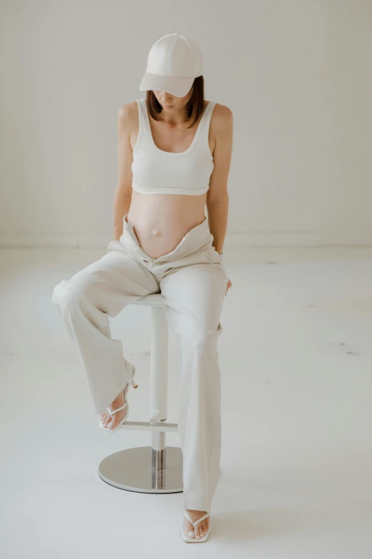 a pregnant woman sitting on a stool in a white room, by Will Ellis, trending on pexels, bare midriff, silver，ivory, pants, textured