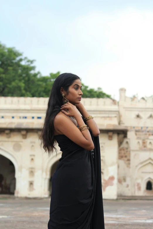 a woman in a black dress standing in front of a building, inspired by Avigdor Arikha, pexels contest winner, black jewellery, at an ancient city, profile image, promotional image