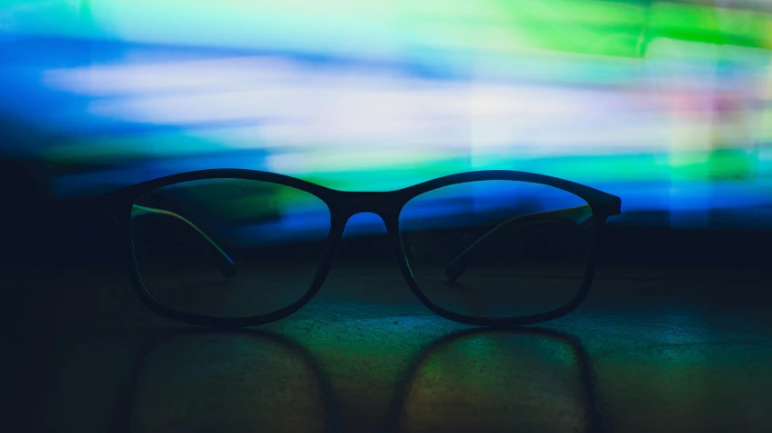 a pair of glasses sitting on top of a table, by Carey Morris, unsplash, visual art, glowing screen, black blue green, abstract lighting, wearing eyeglasses