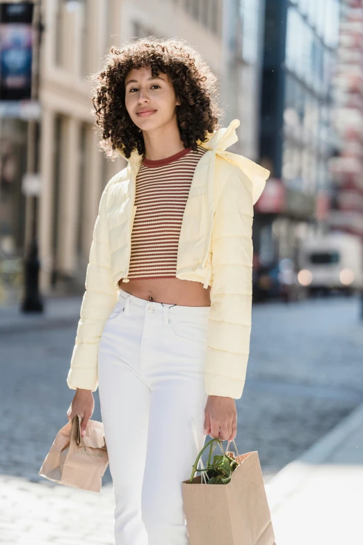 a woman walking down the street carrying shopping bags, inspired by Gina Pellón, trending on pexels, renaissance, wearing yellow croptop, model wears a puffer jacket, light cream and white colors, striped