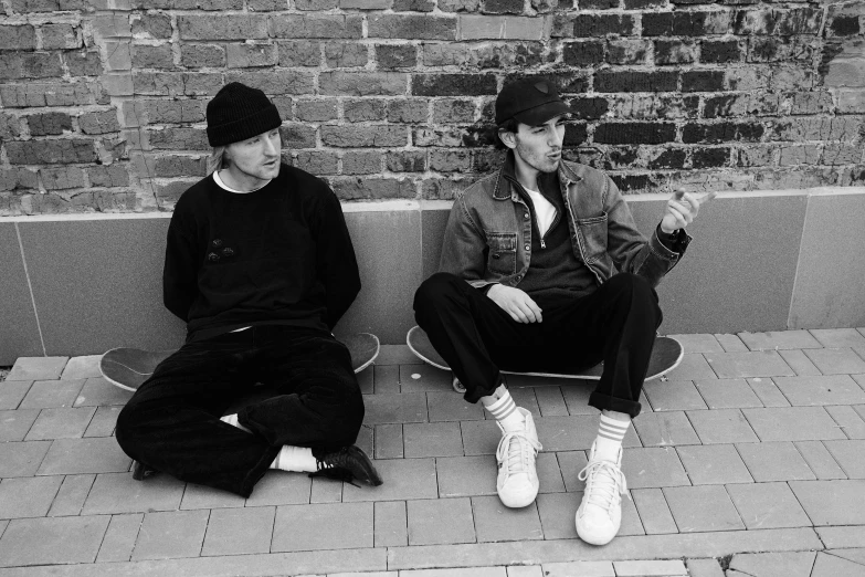 a couple of men sitting next to each other on a sidewalk, a portrait, by Lee Gatch, purism, skateboarding, autechre, promotional image, derek ridgers