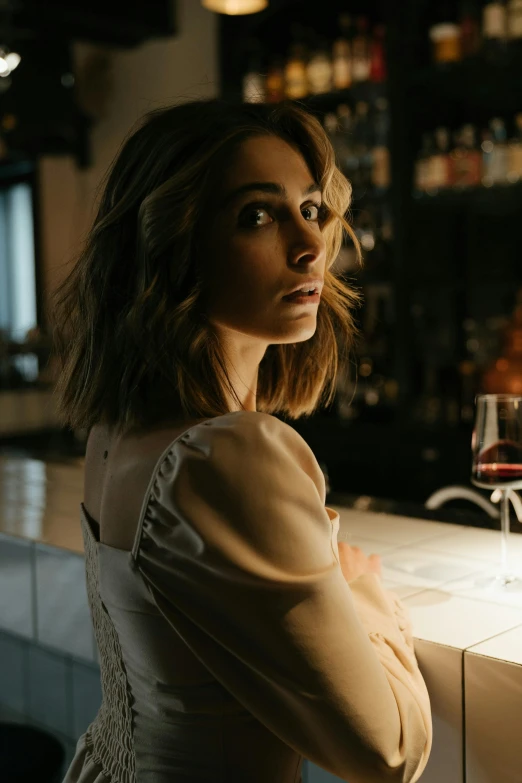 a woman sitting at a bar with a glass of wine, a portrait, inspired by Elsa Bleda, trending on pexels, natalia dyer, mysterious mood, over his shoulder, kiera knightly