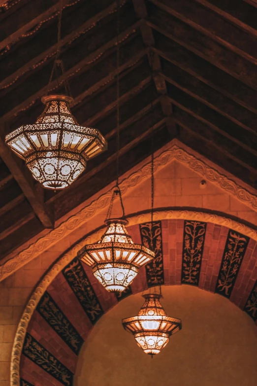 a group of lamps hanging from the ceiling of a building, inspired by Riad Beyrouti, trending on unsplash, arabesque, peaked wooden roofs, hearst castle, cafe lighting, moody details