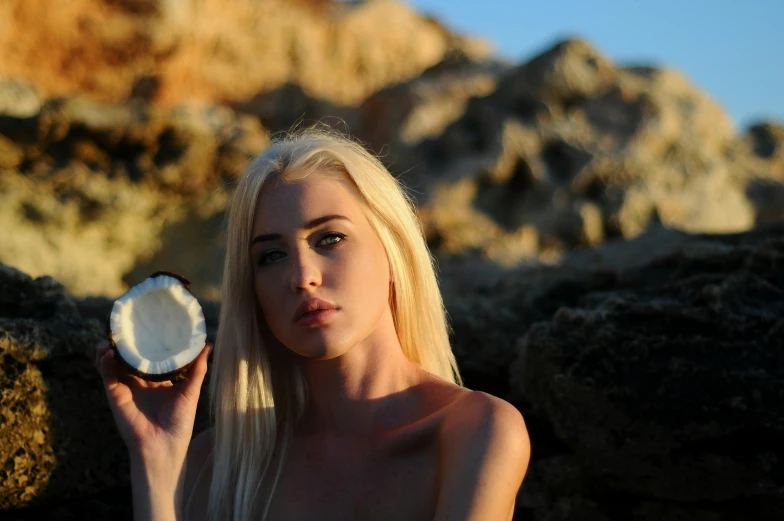 a woman holding a coconut on a rocky beach, a portrait, inspired by Elsa Bleda, unsplash, renaissance, karol bak uhd, pale hair, beauty dish, olive skin