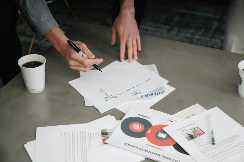 a person sitting at a table with papers and a pen, visuals, bringing people together, promotional material, thumbnail