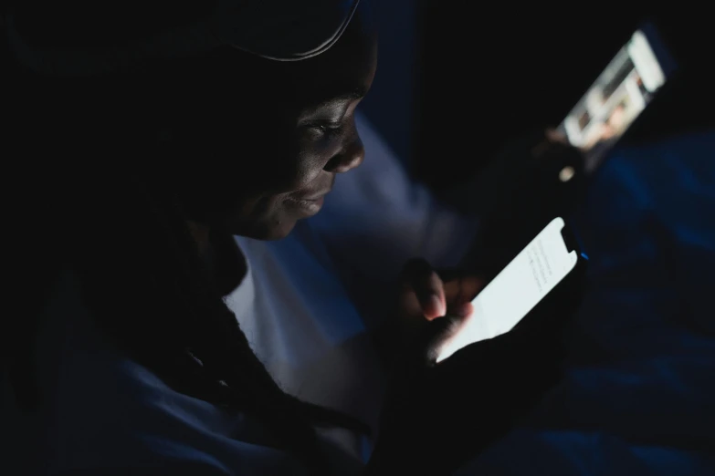 a woman using a tablet computer in the dark, a photo, trending on pexels, afrofuturism, someone sits in bed, he is holding a smartphone, ☁🌪🌙👩🏾, 6 : 3 0 am