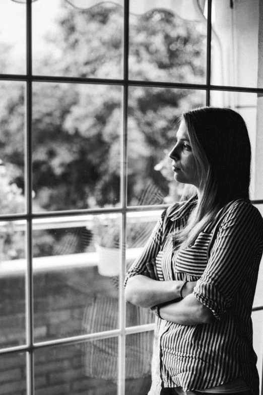 a woman standing in front of a window, a black and white photo, pexels, realism, thoughtful ), arms crossed, concerned, portrait of a 40 years old women