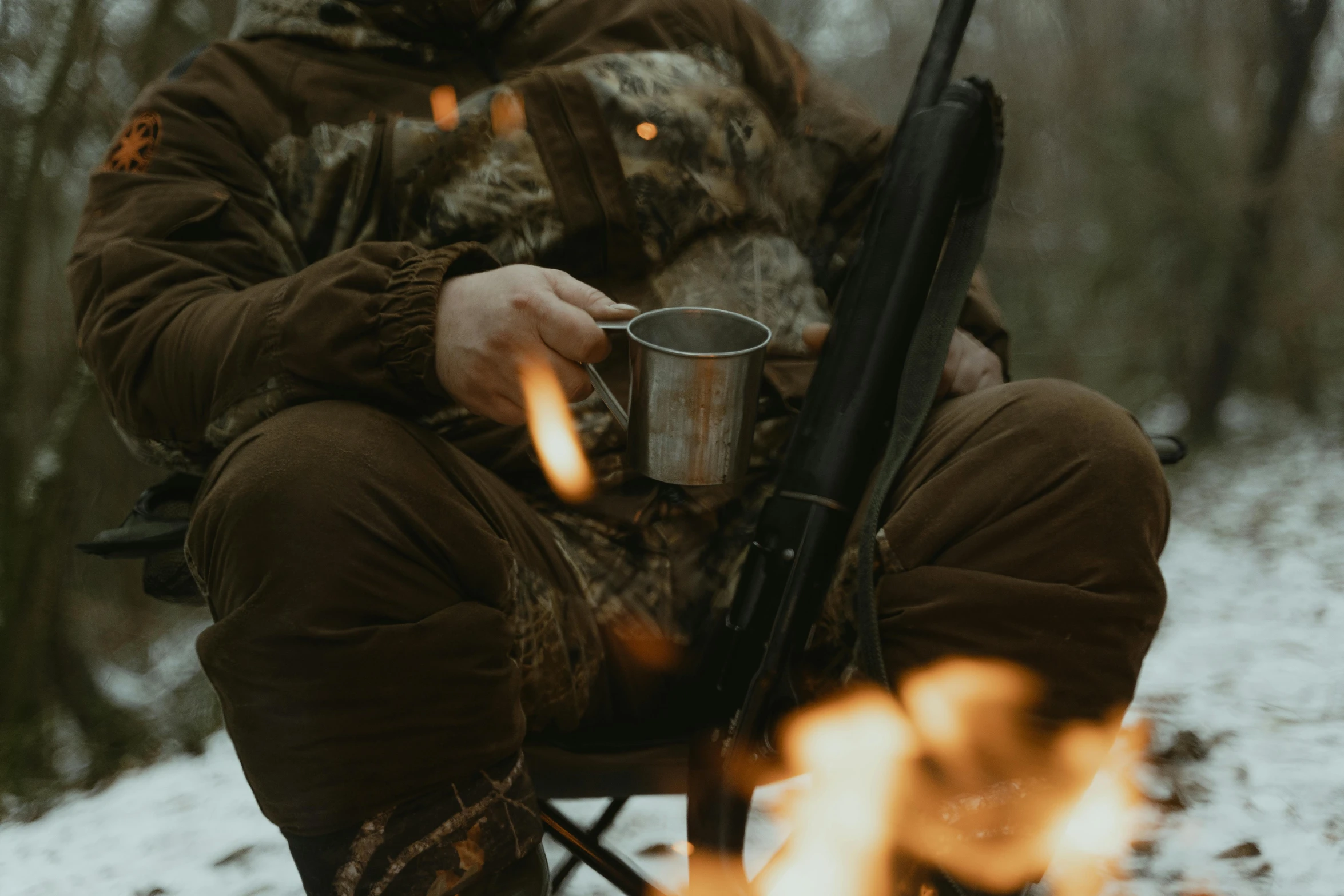 a man sitting on top of a chair next to a fire, hunters gear, next to a cup, brown, thumbnail