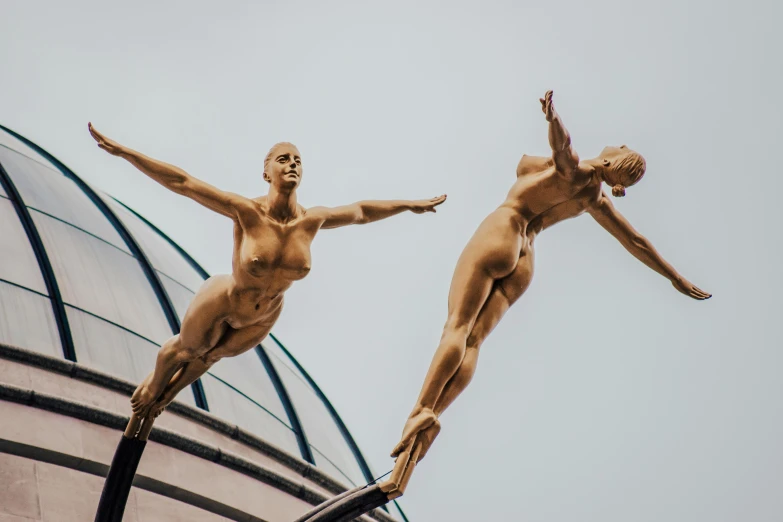 a couple of statues that are on top of a building, an art deco sculpture, by Matija Jama, pexels contest winner, figuration libre, in a gold one piece swimsuit, midair, rendering of beauty pageant, acrobatic