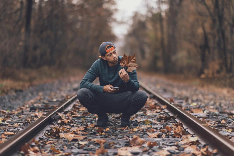 a man kneeling on a train track holding a leaf, pexels contest winner, shooting pose, leaves trap, center focused, profile pic